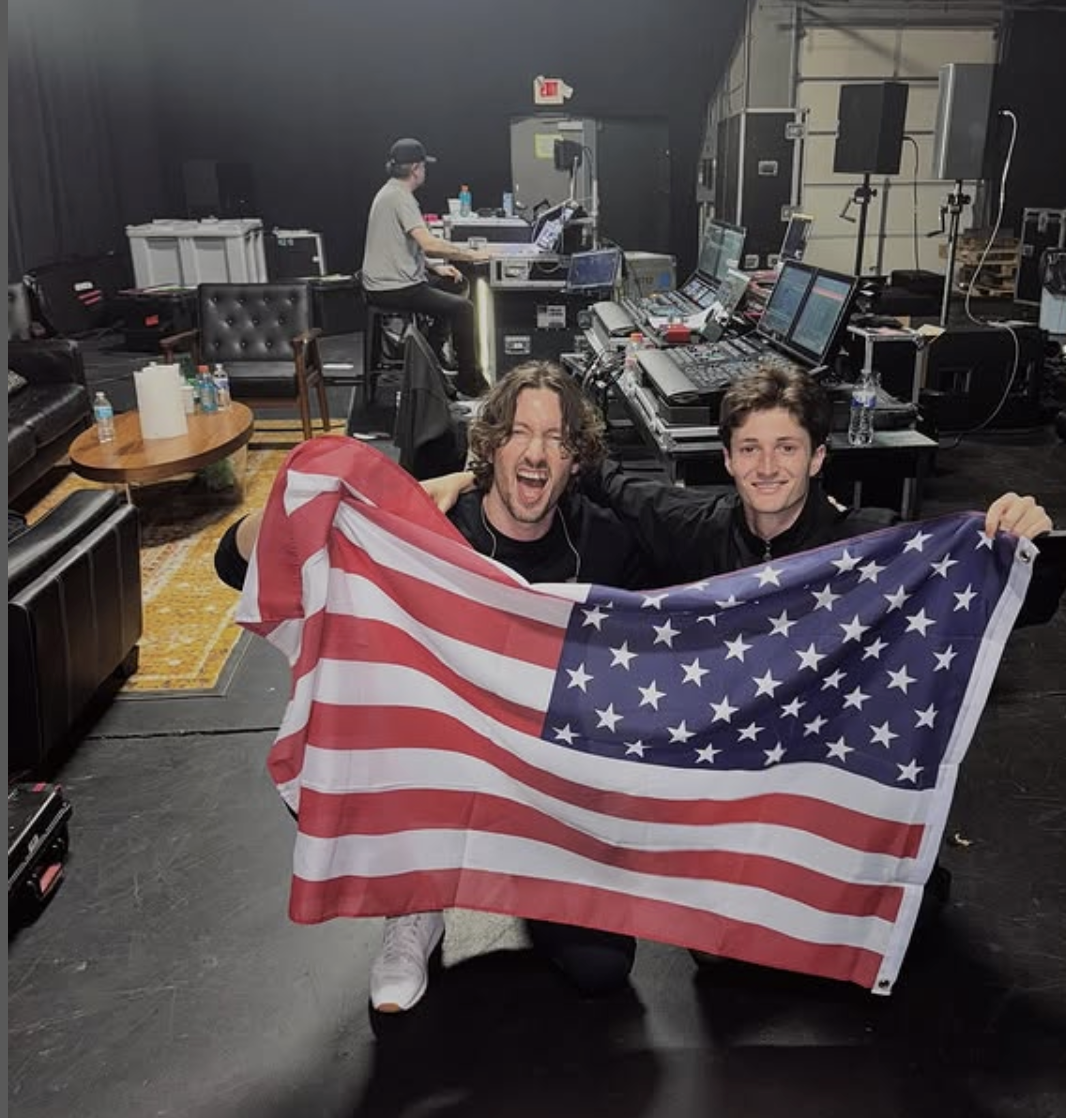Two men holding an American flag in the backstage of a concert venue